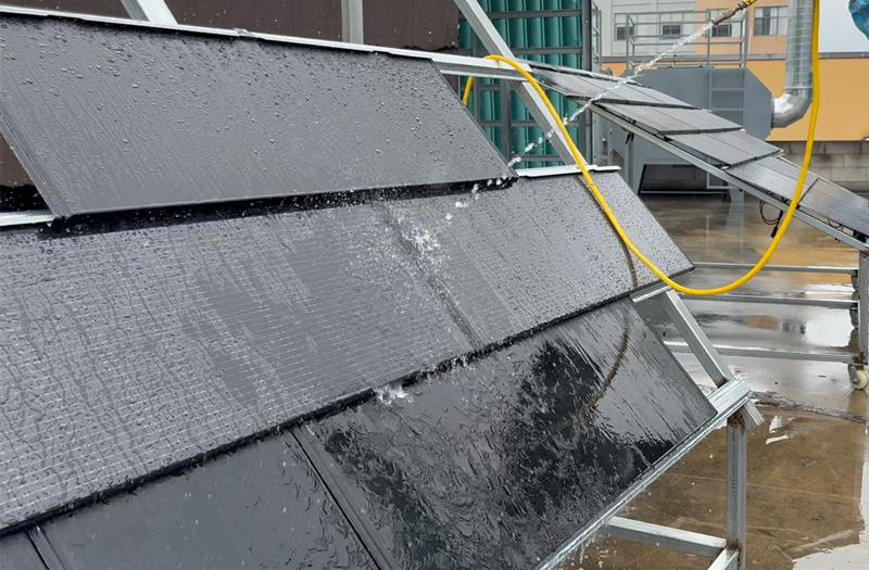 The waterproof performance test of the photovoltaic tile roof is being conducted by using a high-pressure water hose to simulate a rain shower on the solar photovoltaic tiles installed on a sloping roof.