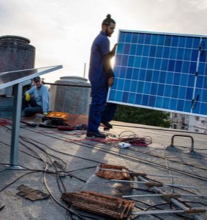 Professional Rooftop Solar Panel Installation and Durable Outdoor Design Professional solar installer carrying a blue solar panel during rooftop installation, showing cables and technical tools on a durable outdoor design project