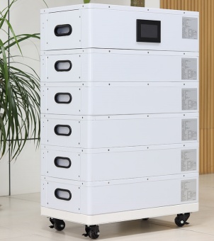 This is a photograph of a home-use stacked energy storage battery system taken in a brightly lit indoor office or home setting. The main subject is a standing, white, multi-layered energy storage unit, its structure composed of six white cuboid modules stacked vertically and compactly. The top layer is the main control module, with a black rectangular LCD smart control display embedded in its center. Below, five identical energy storage battery modules are stacked tightly. Each module has an embedded black racetrack-shaped plastic handle on its left front and a gray-white technical parameter and specification label on its right front. The entire unit is securely placed on a white mobile base, with four industrial casters equipped with black brake locks. A lush, vibrant green indoor foliage plant is visible in the left background, while the right background features a warm, light yellow vertical wooden slat decoration on the wall. The image clearly showcases the clean, modern industrial aesthetics and easily movable structure of the integrated energy storage unit.