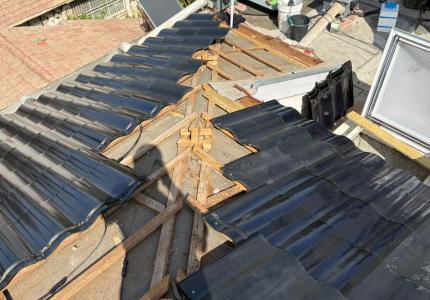 Aerial view of the roof during BIPV installation showing curved solar tiles partially laid on wooden battens with exposed roof structure and construction materials
